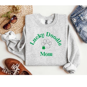 May include: Gray sweatshirt with the text "Lucky Doodle Mom" in green letters. A paw print with a four-leaf clover is in the center of the text.