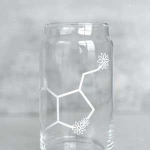 May include: A clear glass drinking glass with a white design of a chemical structure with flowers on it.