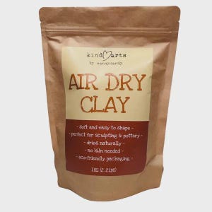May include: A brown paper bag of air dry clay. The label reads "kind arts" and "Air Dry Clay". The bag also states the clay is soft and easy to shape, dries naturally, and requires no kiln. The bag contains 1 KG (2.2 LBS) of clay.