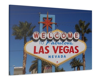 May include: A canvas print of the iconic "Welcome to Fabulous Las Vegas Nevada" sign. The sign is white with red and blue accents, set against a clear blue sky. Palm trees frame the sign, adding to the desert landscape.