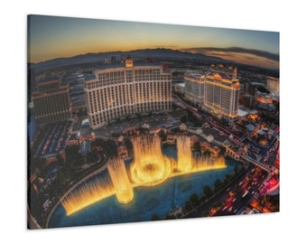 May include: A canvas print of the Las Vegas Strip at dusk. The image features the Bellagio fountains in the foreground, with illuminated buildings and a colorful sky. The print captures the vibrant cityscape and the iconic fountains.