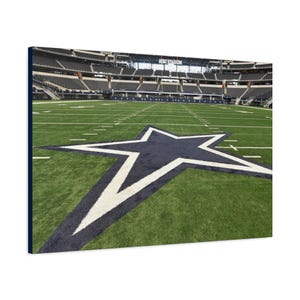 May include: A canvas print of a football field with a large blue and white star at the center. The field is green with white yard lines. The stadium seating is visible in the background, with the text "AT&T STADIUM" above.