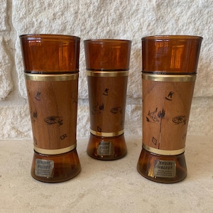 May include: Three amber glass tumblers with a wood-like design and gold trim. Each tumbler has a label that reads "Genuine Walnut" and "Made in Italy".