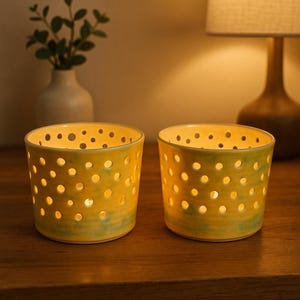Peut inclure: Deux bougeoirs en céramique jaune percés de nombreux petits trous, créant un motif pointillé. Les bougeoirs présentent un effet aquarelle vert à la base. La lueur chaleureuse des bougies illumine les trous, créant une ambiance chaleureuse.