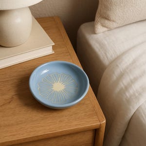 May include: A blue ceramic dish with a white and yellow floral design. The dish is sitting on a wooden nightstand next to a bed.