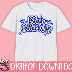 Puede incluir: Camiseta blanca con el texto "Blue Collar Wife" en azul, delineado en azul m&aacute;s oscuro. El dise&ntilde;o incluye corazones azules y detalles de estrellas. La camiseta se muestra sobre un fondo rosa.