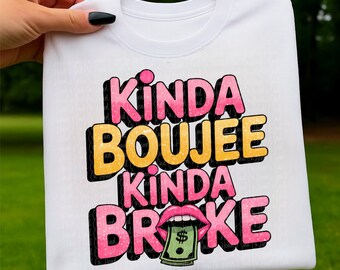 May include: White sweatshirt with the text "Kinda Boujee Kinda Broke" in pink, yellow, and black. The word "Broke" features a graphic of lips holding a dollar bill. The sweatshirt is held by a hand with a black painted nail.