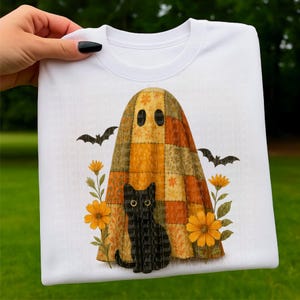 May include: White sweatshirt featuring a Halloween design. The design includes a ghost with a patchwork quilt-like appearance, a black cat, bats, and orange flowers. The cat has the text "Soul Co. Heart" on it.