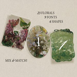 Puede incluir: Tres tarjetas con números de mesa con diseños florales. Una tarjeta rectangular presenta flores moradas y el texto "Table One". Una tarjeta ovalada muestra un campo de flores con el número "1". Una tercera tarjeta tiene un diseño floral verde con el número "1".