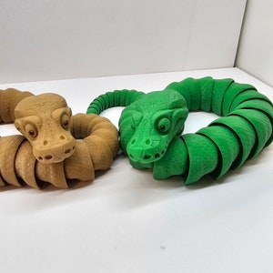 May include: Two segmented snake toys, one brown and one green, are curled into circles. The snakes have detailed faces with eyes and nostrils.