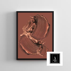 May include: Framed art print featuring two textured brushstrokes in metallic bronze against a terracotta background. The artwork is enclosed in a black frame, with a logo in the bottom right corner.
