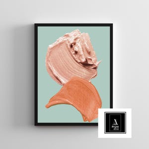 May include: Framed art print featuring two abstract brushstrokes in shades of peach and coral against a light teal background. The artwork is in a black frame and includes a logo in the bottom right corner.