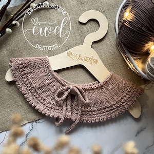 Op de afbeelding: Een delicate roze gebreide kraag met een strikdetail, gepresenteerd op een houten hanger met de tekst "Ewelina Wojsz Ewd Designs" en "Ewelina Design" erop.