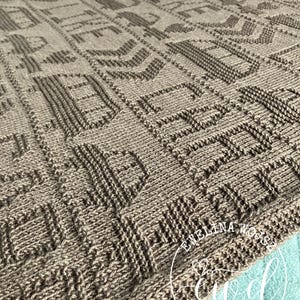 Peut inclure: Gros plan sur une couverture tricotée dans les tons bruns. La couverture présente un motif géométrique répétitif avec des détails texturés. La couverture est faite d'une matière douce et chaude, parfaite pour se blottir. Un article de décoration intérieure douillet.