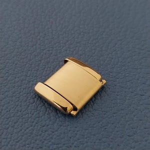 May include: Gold-toned metal watch band link. The link is rectangular with rounded edges and a brushed finish.