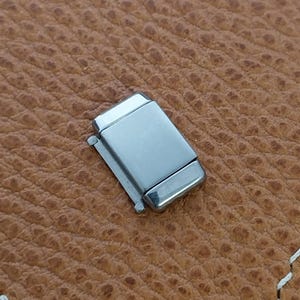 May include: A silver metal watch band clasp. The clasp is rectangular and has a smooth, polished finish.