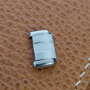 May include: A silver metal watch band link with a brushed finish.