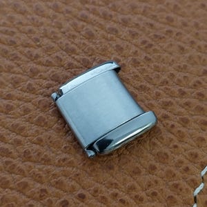 May include: A silver metal watch band clasp with a brushed finish.