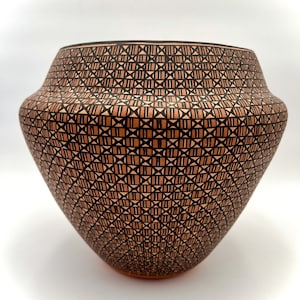 Puede incluir: Un jarrón grande, redondo, de cerámica de terracota con un patrón geométrico de líneas negras y marrones. El jarrón tiene una base ancha y un cuello estrecho.