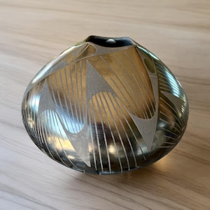 May include: A black and silver ceramic pot with a geometric design. The pot has a rounded shape and a wide opening.