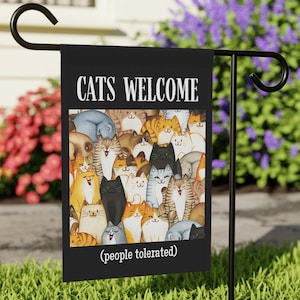 May include: Black garden flag with a white border and the text "CATS WELCOME (people tolerated)". The flag features a colorful illustration of many cats.