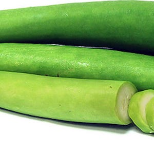May include: Four long, green, smooth, gourd-shaped vegetables, with one sliced into rounds. The vegetables are arranged in a pile on a white background.