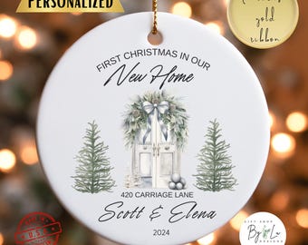 Può includere: Ornamento natalizio rotondo in ceramica bianca con un nastro dorato. L'ornamento presenta un'illustrazione ad acquerello di una porta d'ingresso con una ghirlanda, due alberi e il testo "First Christmas in Our New Home". Include i nomi "Scott & Elena" e l'anno 2024.