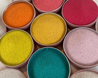 May include: Assortment of colourful sand in small round containers. The colours include orange, yellow, teal, pink, and red.