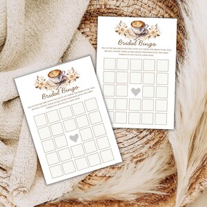May include: Two white Bridal Bingo game cards with a coffee cup and floral design. The cards have a grid of squares and the text "Bridal Bingo". The cards are on a woven surface.
