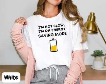 Pode incluir: Camiseta branca com o texto "I'm not slow, I'm on energy saving mode" e um ícone de bateria amarelo.
