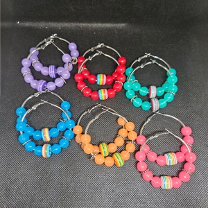 Peut inclure: Six paires de boucles d'oreilles créoles avec des perles colorées. Chaque paire a une seule grosse perle avec un motif de rayures arc-en-ciel.