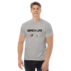 May include: A heather grey t-shirt with the text "BEACH LIFE" printed in black. The shirt features a small graphic of a seashell and a lit match.