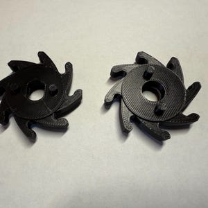 Könnte beinhalten: Zwei schwarze Kunststoffzahnräder mit einem Sternmuster und einem zentralen Loch. Die Zahnräder haben eine strukturierte Oberfläche und sind so konzipiert, dass sie ineinandergreifen.