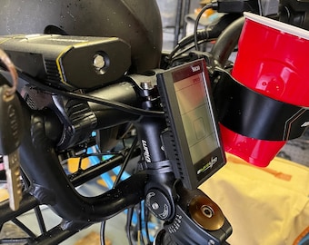 May include: A black bicycle handlebar with a black and silver bike computer, a black and yellow light, and a red cup holder. The bike computer displays the text "SPEED" and the number "56.50".