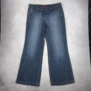 Può includere: Jeans blu in denim con un design a gamba larga. I jeans hanno un classico stile a cinque tasche, una chiusura con bottone e cerniera e un lavaggio sbiadito. Realizzati in resistente tessuto denim.