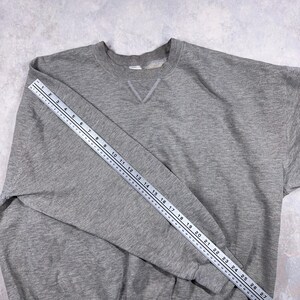 May include: A heather gray sweatshirt with a crew neck and a V-shaped detail at the neckline. A ruler is placed across the sleeve, measuring approximately 27 inches. The sweatshirt is made of a soft, comfortable material.
