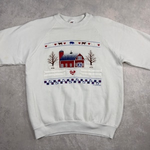 May include: White sweatshirt with a colorful farm scene. The design features a red barn with a blue roof, trees, and a white fence. Above the barn are hearts, cows, and pigs. The words "Country Wishes" are on the design.