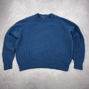 May include: A teal crew neck sweater with a ribbed knit pattern. The sweater features long sleeves and a classic fit. The brand name "Gasser Scott" is visible on the neck label. The sweater is made of a soft, warm material.