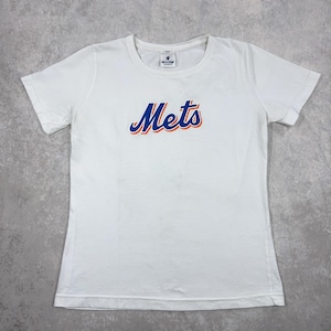 May include: White t-shirt with the word "Mets" in blue script with an orange outline. The shirt has short sleeves and a crew neck. The Mets logo is centered on the front of the shirt.