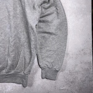 May include: Close-up of a heather gray sweatshirt. The image shows the sleeve and part of the body of the garment. The cuff is ribbed, and the fabric appears to be a soft, comfortable material. The background is a mottled gray.