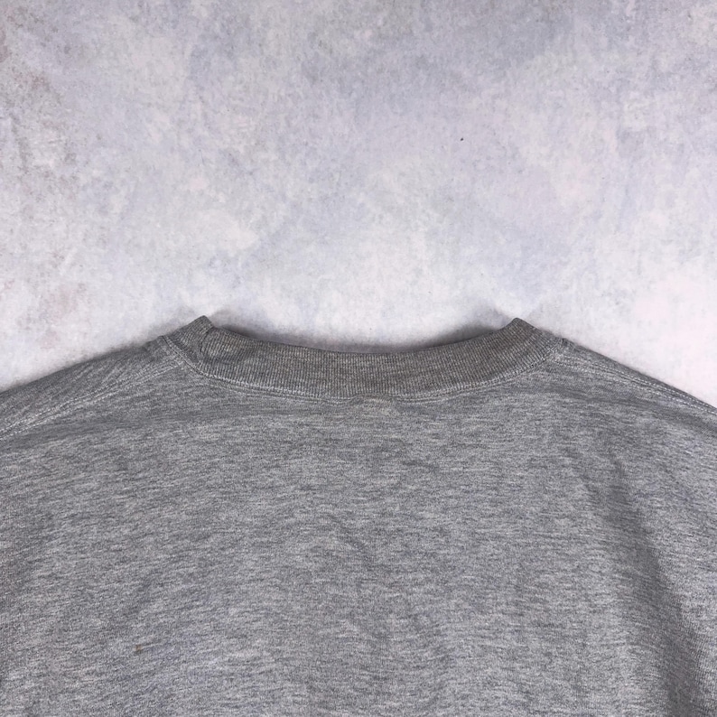 May include: A heather gray crew neck sweatshirt. The neckline is ribbed and the body of the shirt is a solid gray color. The fabric appears to be a soft, comfortable material.