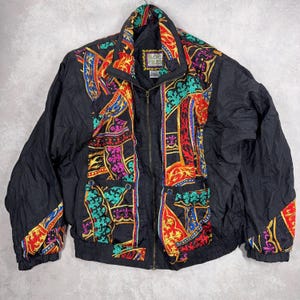 May include: Black vintage jacket with a colorful patterned design. The jacket features a high collar, a zipper closure, and pockets. The pattern includes red, blue, green, and gold accents. The jacket has the text "ROC CREST" on a label.