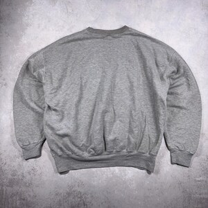 May include: A heather gray sweatshirt with a crew neck, long sleeves, and ribbed cuffs and hem. The casual top is made of a soft material and is suitable for everyday wear. The sweatshirt is a versatile piece for a relaxed style.