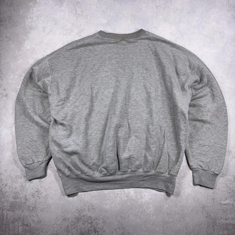 May include: A heather gray sweatshirt with a crew neck, long sleeves, and ribbed cuffs and hem. The casual top is made of a soft material and is suitable for everyday wear. The sweatshirt is a versatile piece for a relaxed style.