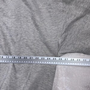 May include: A close-up of a gray t-shirt with a measuring tape across the bottom. The tape measures from 16 to 30 inches. The shirt is a solid color and appears to be made of a soft material.