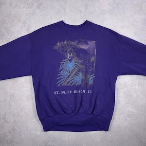 May include: Purple sweatshirt with a graphic of a parrot and tropical foliage. The graphic is in shades of blue, green, and gold. The text "ST. PETE BEACH, FL" is printed below the graphic.