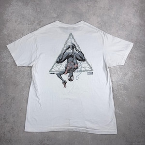 May include: White t-shirt featuring a graphic of Spider-Man hanging upside down within a triangular web design. The design includes the text "HUF" and "MARVEL".