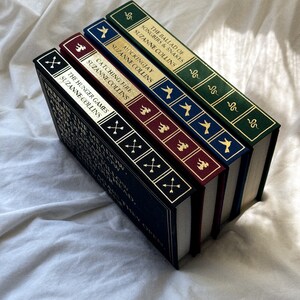 May include: A stack of five hardcover books with gold lettering and illustrations on the spines. The titles are "The Hunger Games", "Catching Fire", "Mockingjay", "The Ballad of Songbirds and Snakes", and "The Hunger Games".