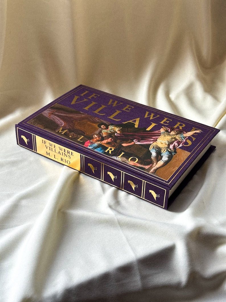 May include: A purple hardback book with gold lettering titled "If We Were Villains" by M.L. Rio. The cover features a painting of a group of people in a dramatic scene.