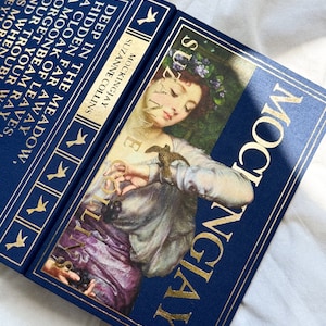 May include: A blue hardcover book with gold lettering titled "Mockingjay" by Suzanne Collins. The cover features a painting of a woman with a bird in her hand.